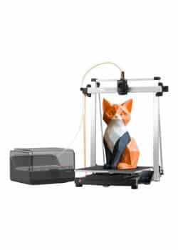 An Anycubic Kobra 3 Max Combo 3D printer, primarily gray and white, with an orange and black segmented fox figurine on its print bed. An external filament box with tubing is connected to the printer on the left.