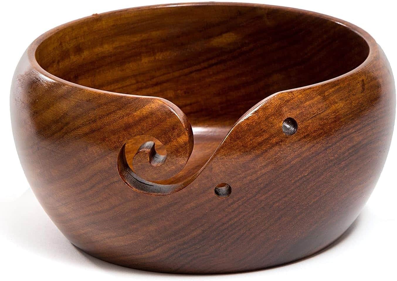 Handmade wooden yarn bowl with spiral cutout holding colorful yarn with crochet hook